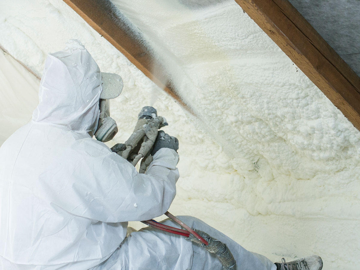 Technician spraying foam insulation on attic wall